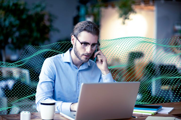 Young business man working on laptop talking on smartphone.